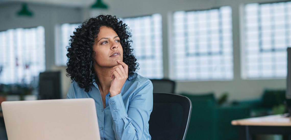 woman of colour thinking at desk with laptop