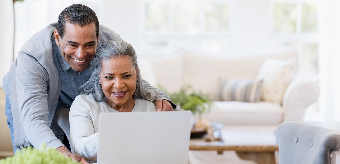 elderly-couple-smiling-looking-at-finances-on-laptop